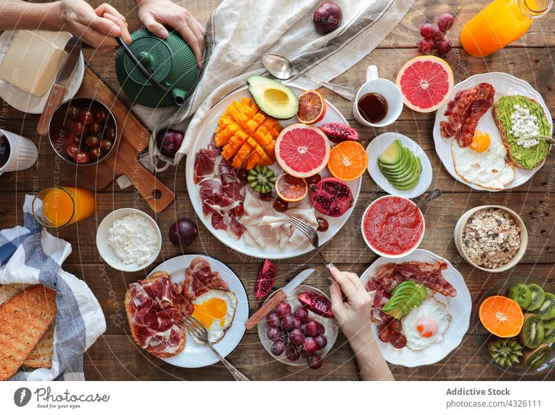 Top view of healthy breakfast hands serving avocado tomato fried eggs ham papaya pomegranate kiwi grapes bacon brunch grapefruit turkey toasts bread toasted