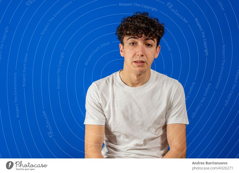 Portrait Of A Serious Young Man Standing On Blue Background man portrait curly face guy background blue person young male isolated handsome studio fashion
