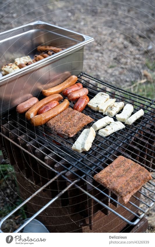 Barbequing sausages on hot coals outside, two grills with meat, cheese and sausages haloumi haloumni grilled cheese barbeque barbecue bbq tongs turn turning