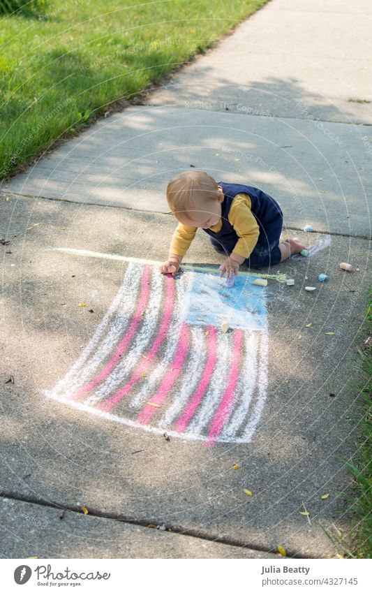 One year old baby next to chalk drawing of the American flag; toddler is crawling and playing with chalk on the 4th of July 4th of july american flag usa