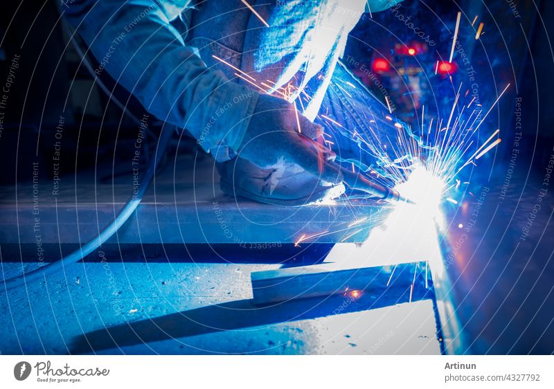 Welder welding metal with argon arc welding machine and has welding sparks. A man wears protective gloves. Safety in industrial workplace. Welder working with safety. Worker in steel industry factory.