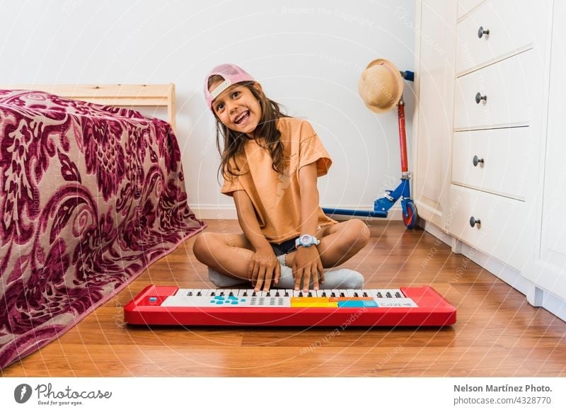 Happy hispanic girl wearing a pink cup playing in a red piano in her bedroom pianist person chord classical finger rythm create practicing performance melody