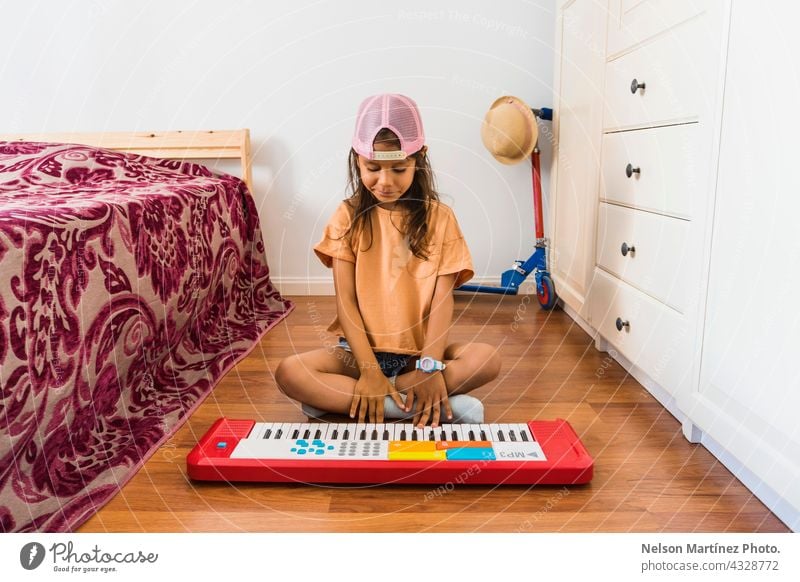 Little hispanic girl wearing a pink cup playing in a red piano in her bedroom pianist person chord classical finger rythm create practicing performance melody