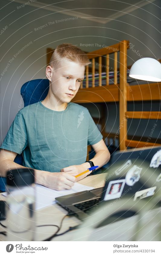 Young man writing in notebook. student studying online home working young dormitory programmer education college laptop boy teenager 14-15 caucasian blond white