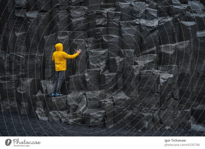 Adult man in yellow jacket standing on basalt columns on Reynisfjara Black Sand Beach in Iceland iceland reynisfjara sand beach black adult nature volcanic vik