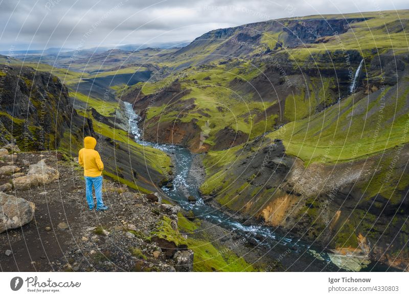 Aerial view of man enjoying Iceland landscape of highland valley and river Fossa with blue water stream and green hills and moss covered cliffs aerial above