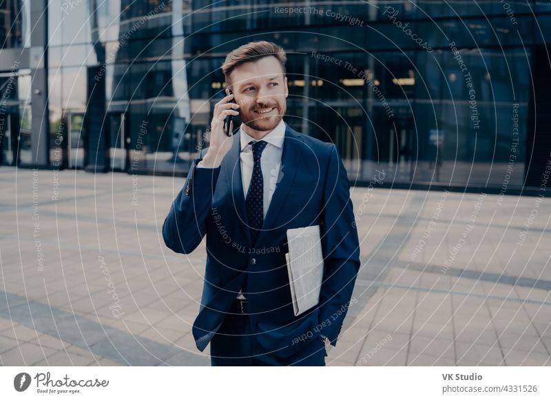 Happy office worker with newspaper talking on smartphone handsome businessman mobile call happy good smiling male blue news. hearing success. newspaper suit