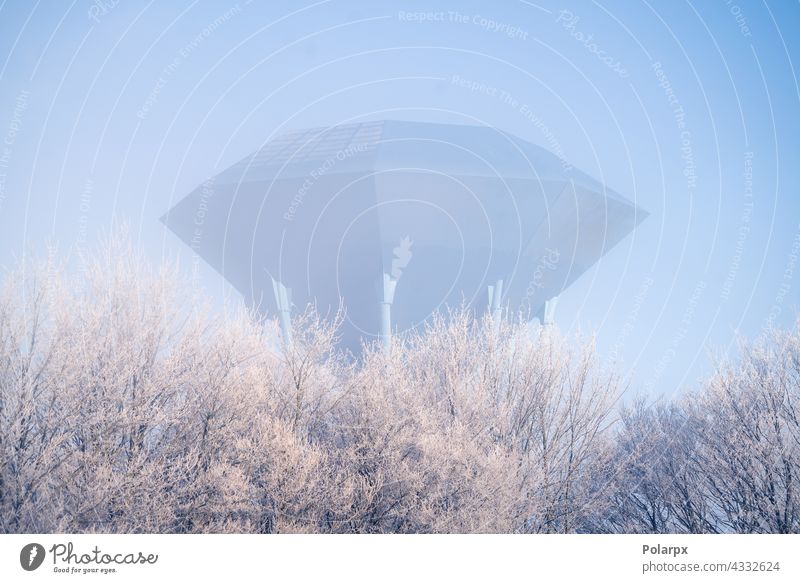 Futuristic water supply tower on cold morning day urban gallon consumption preserve aqua water tank misty fog utility object trees snow winter frost future