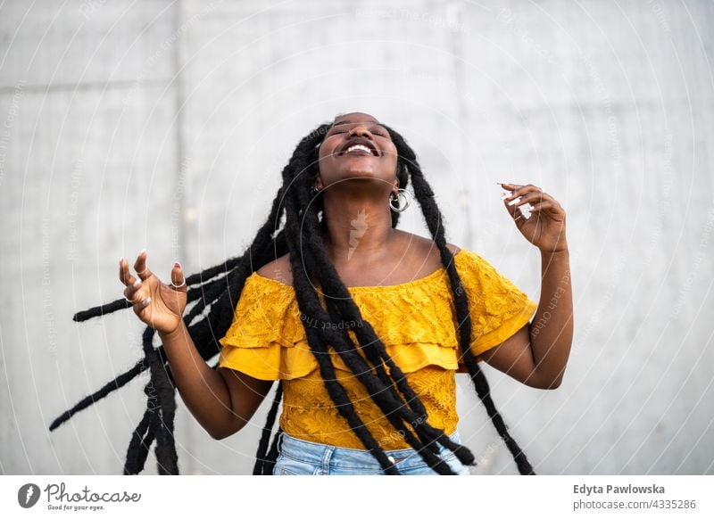 Beautiful young woman dancing in front of gray wall dreadlocks proud real people city life African american afro american Black ethnicity sunny sunset outside