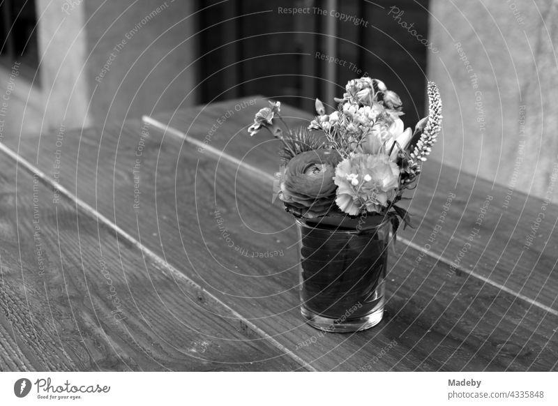 Simple drinking glass with flower decoration on a wooden table in front of a café in Braubachstraße in Frankfurt am Main in Hesse, photographed in neo-realistic black and white