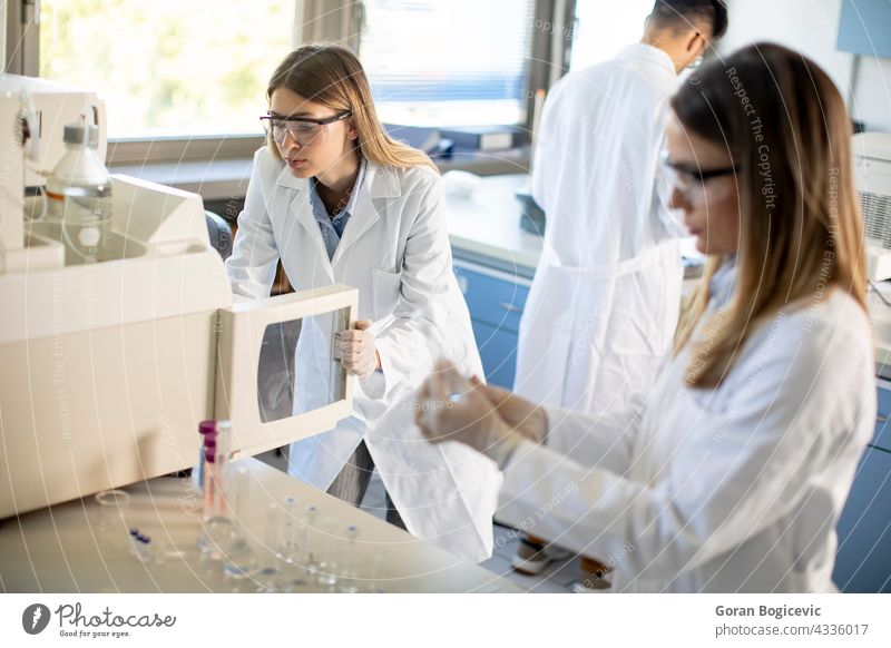 Female scientists in a white lab coat putting vial with a sample for an analysis on a ionchromatography system in biomedical lab automatic biochemistry