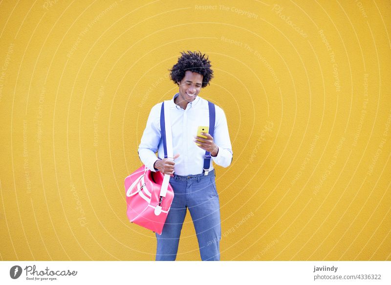 Black man with afro hairstyle carrying a sports bag and smartphone in yellow background. businessman black curly guy african portrait young smile commuter