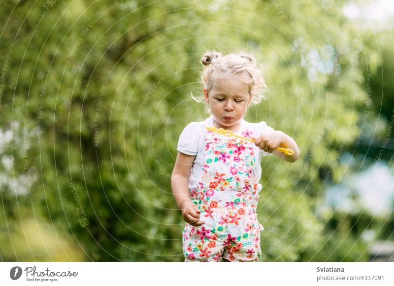 A little girl catches soap bubbles in the park, sitting on the