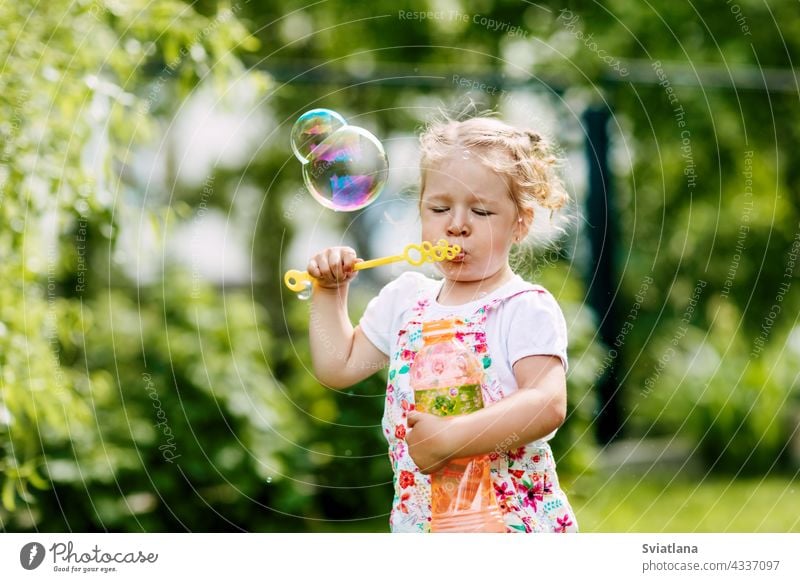 A little girl blows soap bubbles in the park. Happy childhood, summer time. Side view joy baby green fun portrait beautiful kid play cute nature funny blowing