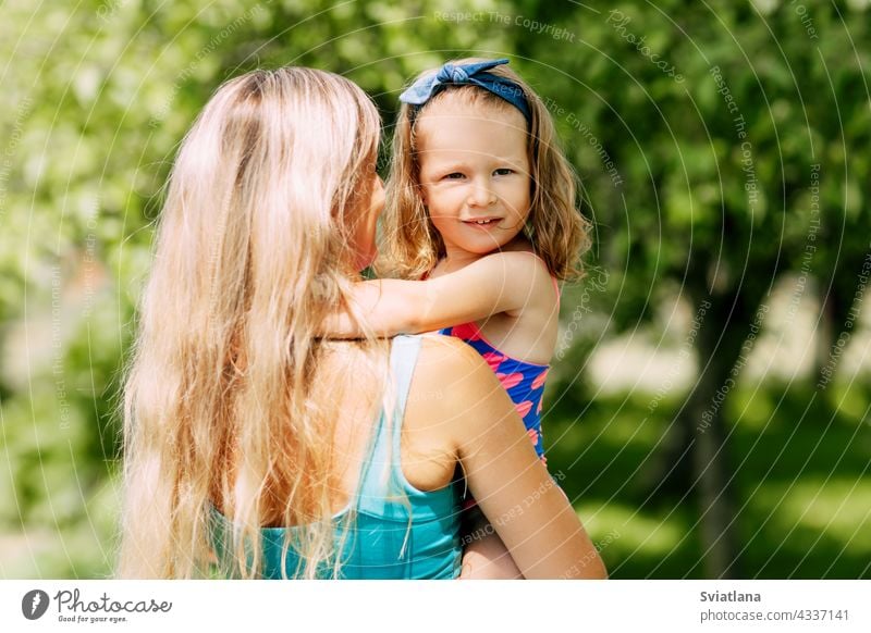 A young mother holds her little daughter in her arms on a summer day in the garden or park family parent mom child childhood happy togetherness motherhood care