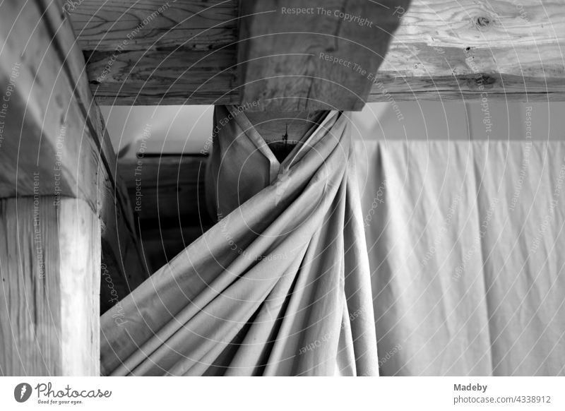 Massive old wooden roof beams under the roof and a curtain with folds in a renovated farmhouse on a farm in Rudersau near Rottenbuch in Upper Bavaria, photographed in traditional black and white