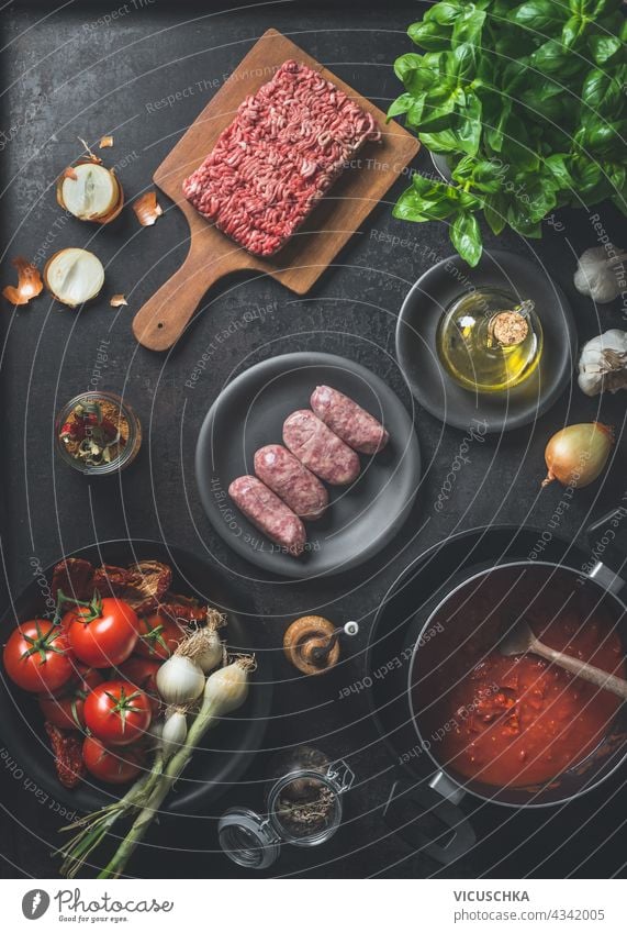 Various ingredients for Sauce bolognese : Salsiccia sausages, minced meat, tomatoes sauce, herbs and spices on dark kitchen background. Top view. Cooking preparation