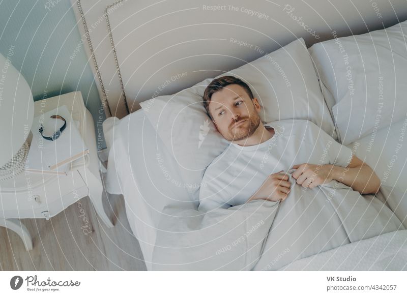 Handsome stressed young caucasian male lying in bed with his eyes open man sleep bedroom insomnia tired restless pillow indoor home adult worried awake bedtime