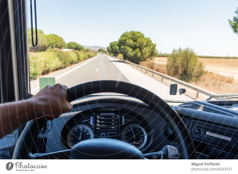 View that a truck driver has from his workplace, with one hand gripping the steering wheel, the dashboard with job information and the road in the background.
