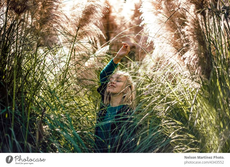 Portrait of a beautiful blonde woman around the plants outdoors serene style confidence happy relax solitary girl holding green bunch carefree self-assured