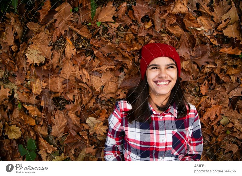 Laughing teen girl lying in a bed of dry leaves in autumn happy smile laughing joy fun positive cheerful copy space eyes toothy dreamer fall playful funny cute