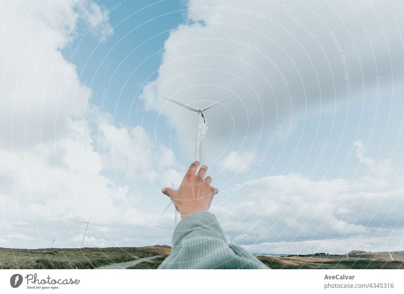 Human hand reaching Wind Turbines Windmill Energy on the nature, during a super sunny day, with copy space and a lot of air electricity power renewable turbine