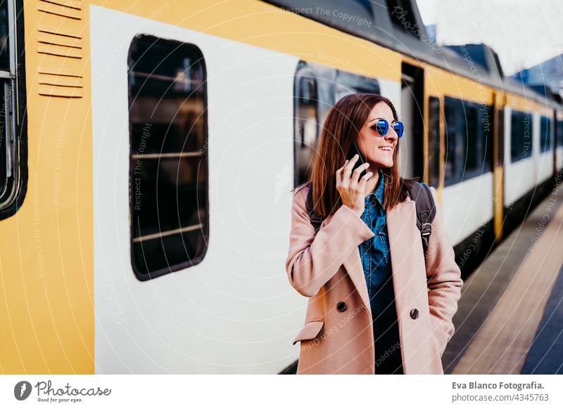 happy backpacker caucasian woman at platform on train station talking on mobile phone. Travel concept travel technology daytime Porto arrival baggage beautiful