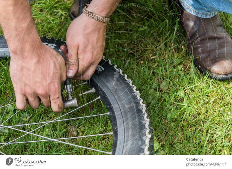 Hands put air pump on the valve of a bicycle tire hands Handcrafts Air pump Bicycle Bicycle tyre Spokes Wheel rim Boots jeans Grass Plant Day daylight Close-up