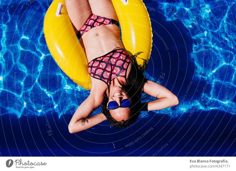 top view of happy caucasian woman floating on yellow donuts inflatable at swimming pool. Summer time, vacation and lifestyle summer sunglasses fun beach slim