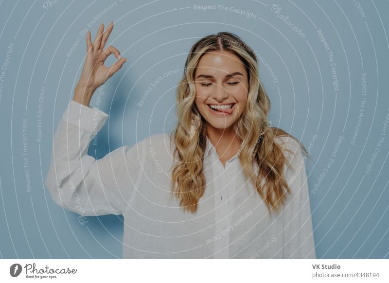 Crazy blonde woman making ok gesture while showing tongue crazy funny young okay silly facial expression closed eyes joyful cheerful face isolated lady lips