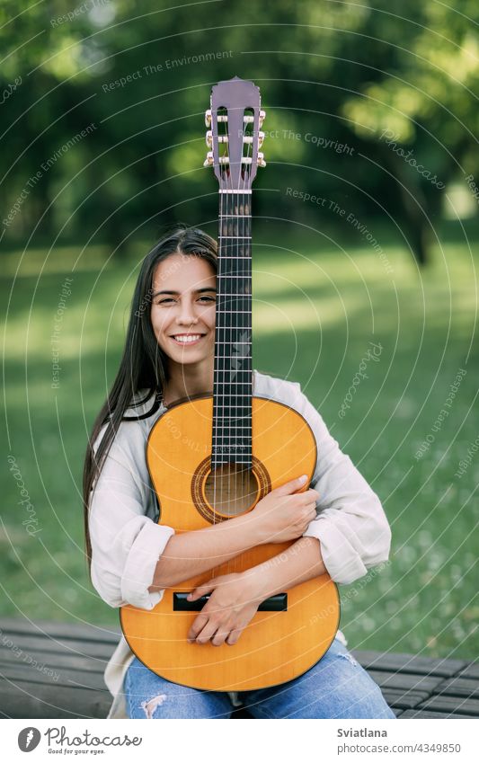 Portrait of a young girl guitarist who smiles and holds a guitar in her hands. Girl-musician, music, hobby park portrait creative lifestyle female woman