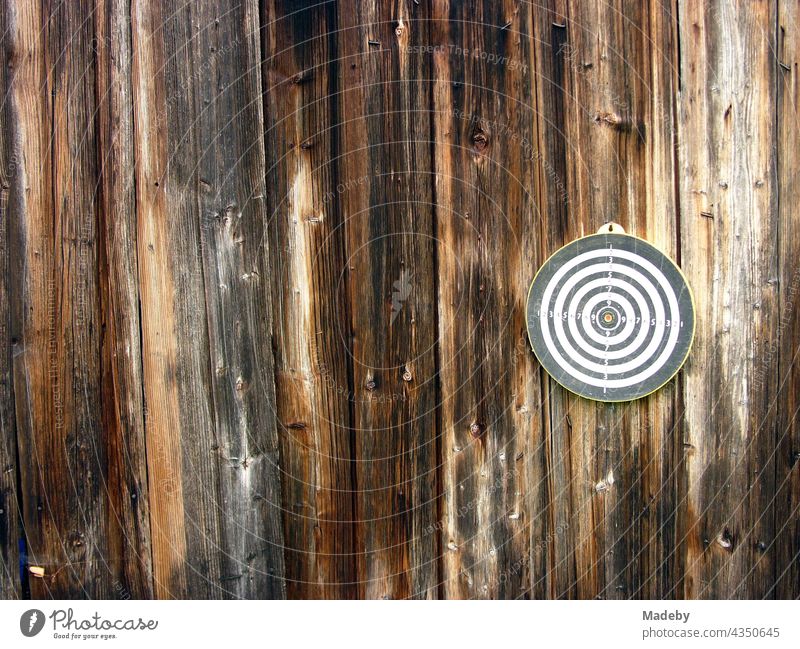 Round dartboard for playing darts on the brown wood of the facade of an old barn on a farm in Rudersau near Rottenbuch in the district of Weilheim-Schongau in Upper Bavaria