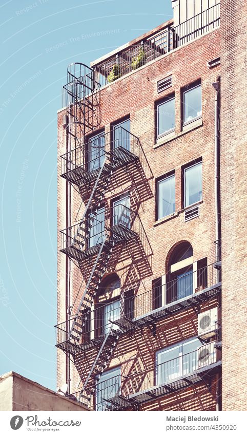 Old brick building with fire escape in New York City, color toning applied, USA. NYC townhouse city old Manhattan retro vintage stairs apartment urban