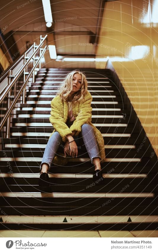 Portrait of a blonde caucasian woman on the stairs of a train station fashion lifestyle casual coat yellow Lifestyle Woman Style young attractive indoors