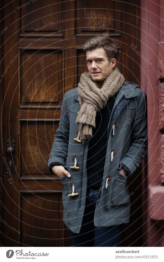 young man with duffle coat waits in the house entrance Young man Wait front door Entrance Winter Coat winter jacket Scarf Blonde Stand Lean