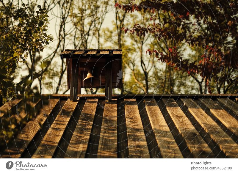 Bell on wooden roof of a chapel pediment Wood Wooden roof Roof Pattern trees bushes Sky Warm light morning light Morning Light Shadow Nature Exterior shot