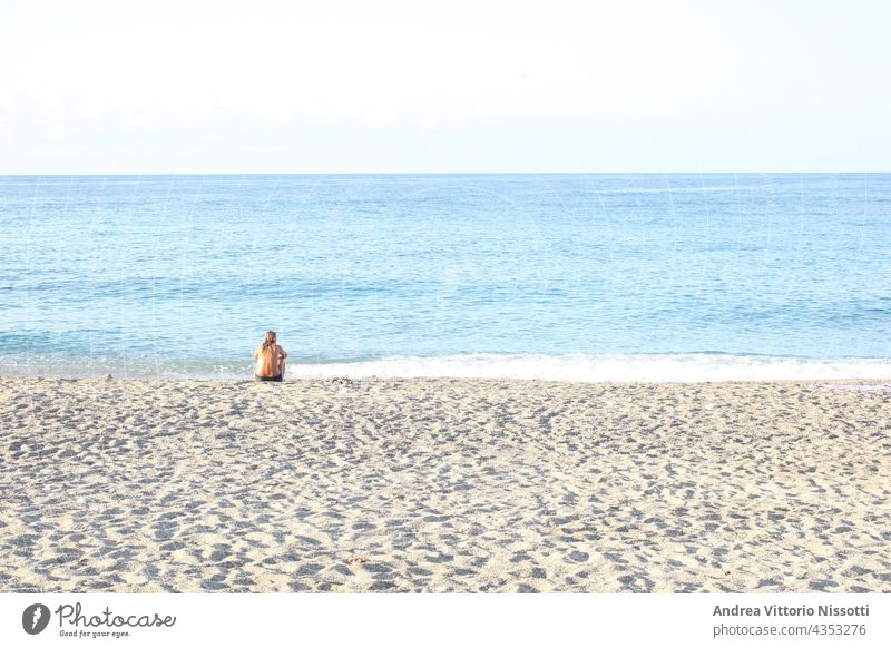 Woman sitting alone on a beach contemplating the sea with copy space for your text horizontal color image people caucasian outdoor seaside summer holiday