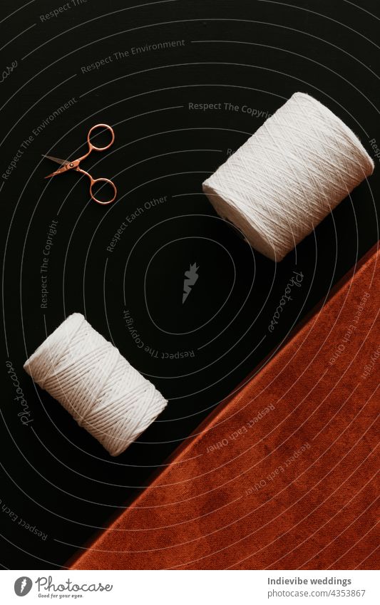 Two rolls of cotton rope, a gold rose scissors and an orange color canvas on black background. brown rust string thread creative diy hand-made needle sewing