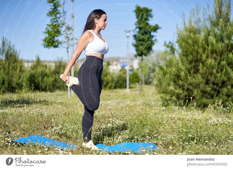 young woman doing gymnastic exercises on the grass. Female model in sportswear pretty female outside fitness training stretching athlete exercising wellness