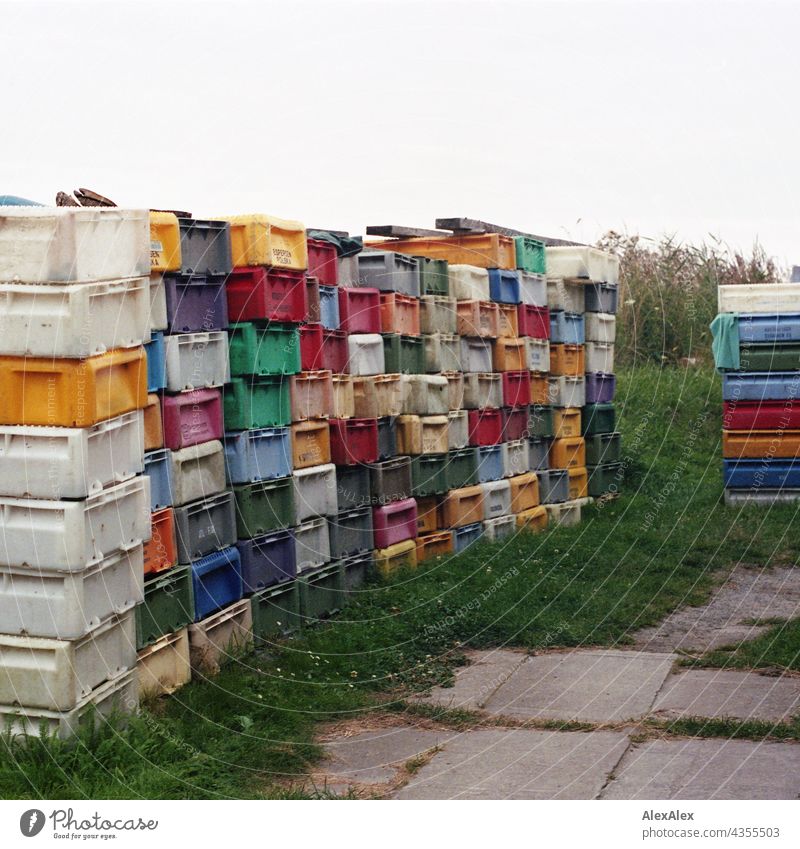 Fishboxes- Tetris- Mosaic - stacked, colorful fishboxes on a piece of grass next to the road Fish bin Crate plastic Plastic variegated Stack crooked and crooked