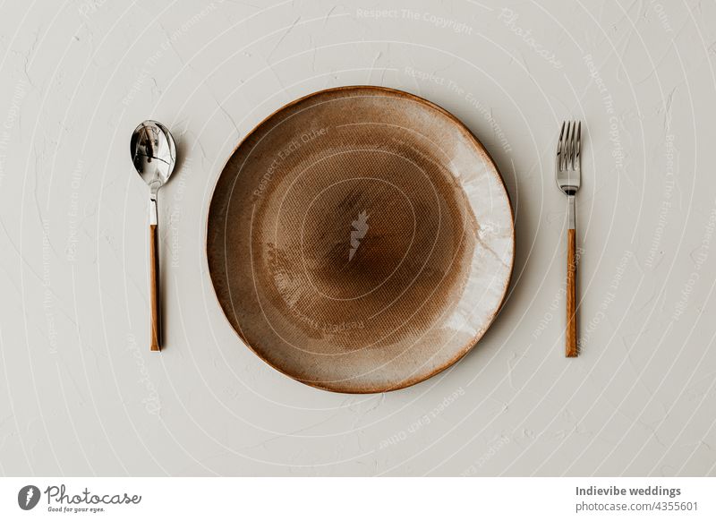 A brown plate with a spoon and a fork on beige background. Flat lay, top view. Brown and natural color plates. Textured grainy pattern on the plates. art bowl