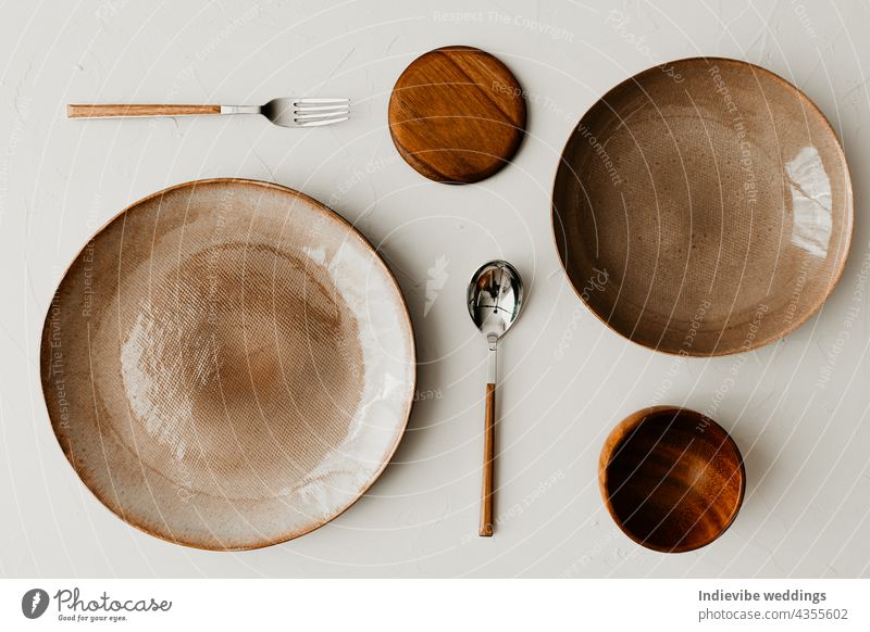 Two different size plate with a spoon and fork on beige background. Flat lay, top view. Brown and natural color plates. Textured grainy pattern on the plates.