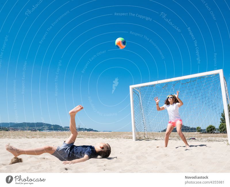 two children playing soccer on beach football happy water cheerful friendliness shore ocean summer casual sea together joy closeness smiling vacation sport