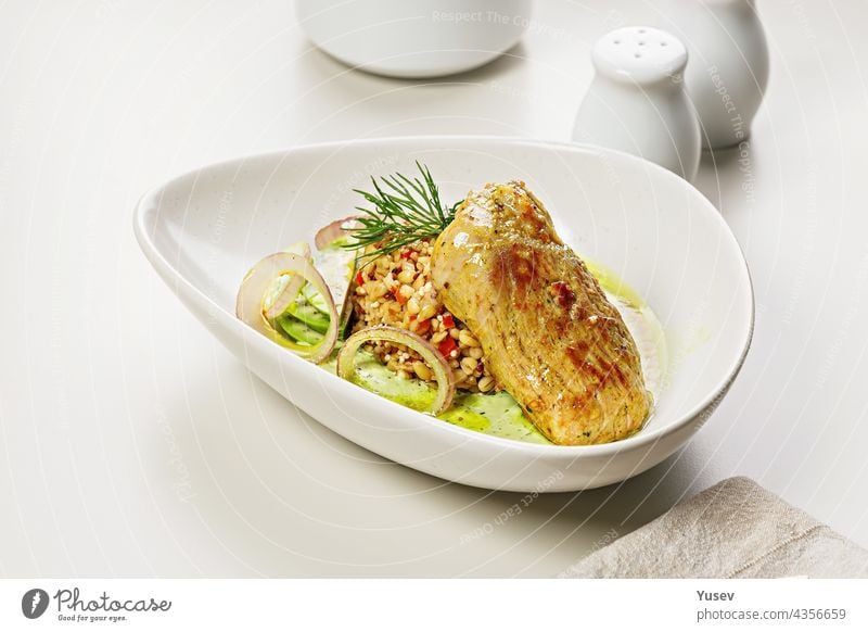 Turkey fillet with garnish and sauce. Baked turkey with bulgur, quinoa and vegetables. Restaurant dish. Cooked poultry with garnish. Food styling and food photography. Copy space. Light background