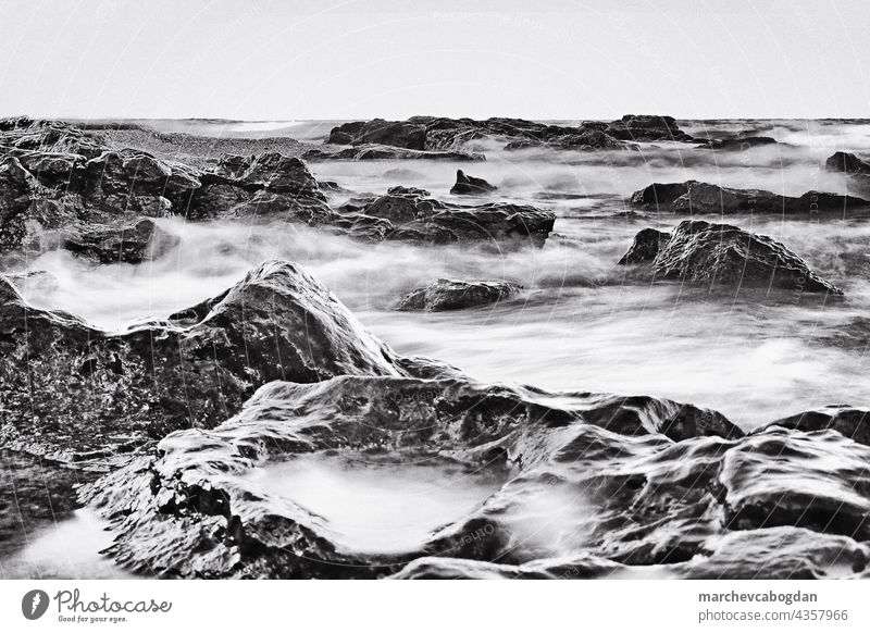 Long exposure of the ocean flowing over large pebbles. Monochrome image. rock nature long exposure water coast landscape wave detail beach stone texture