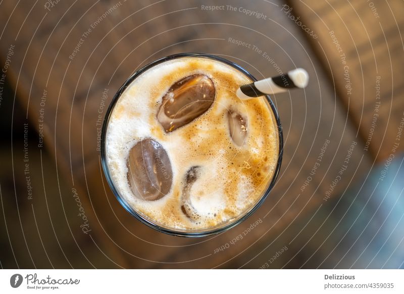 Top down view of a ice latte coffee with a straw on a wooden table coffee latte milk cold drink ice cube ice cubes cafe cafeteria caffeine closeup background
