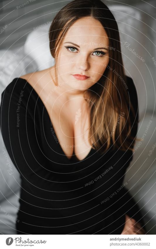 girl in a black dress with a large neckline posing on a white sofa - a  Royalty Free Stock Photo from Photocase