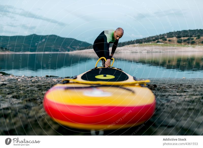 Man pumping paddleboard before surfing man sup sup board surfer prepare seashore wetsuit beach male surfboard sport ocean water seaside water sports waterfront