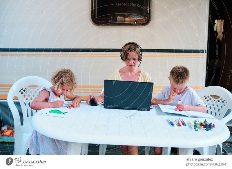 a family in a caravan at a camping. Mother working and children having a leisure time drawing holiday summer business woman people laptop young boy internet