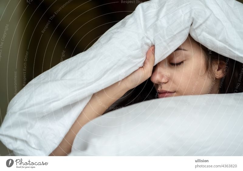 Portrait of an attractive, young, sexy dark haired woman in Bed, hand and head on the pillow under the blanket, Copy space. Sleep sleeping people bed white